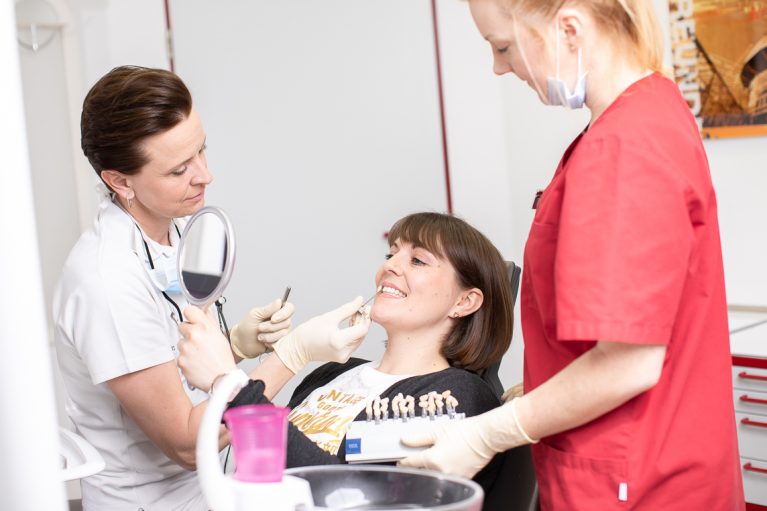 Dr. Verena Mönnich zeigt Patientin Zahnfarben, an Ihren Zähnen, vor einem Spiegel